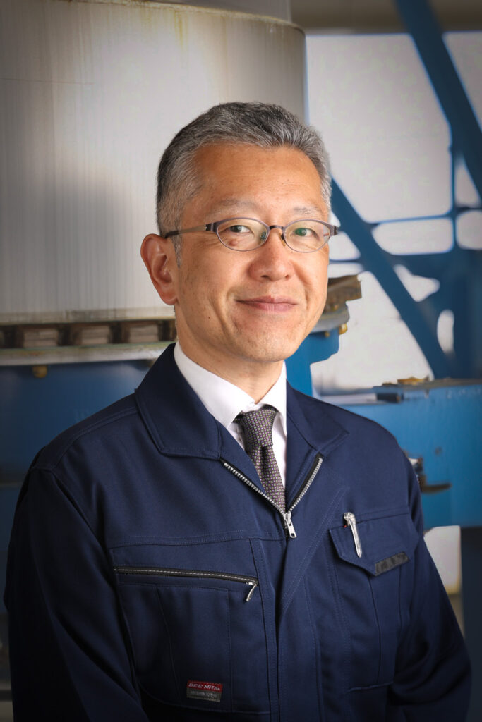 大塚社会保険労務士事務所代表の大塚陽太郎の画像。作業着を着用し、工場内でこちらに笑いかけている様子